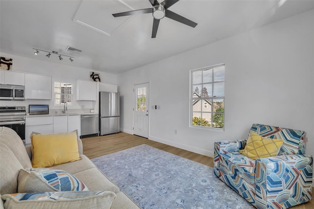 living room with rail lighting, attic access, ceiling fan, light wood-type flooring, and baseboards