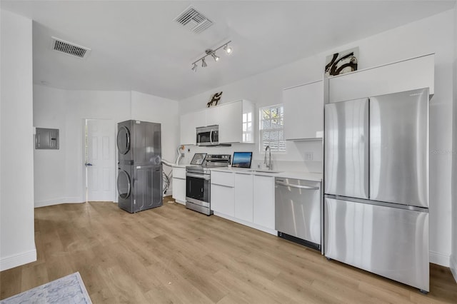 kitchen with stainless steel appliances, visible vents, white cabinets, light countertops, and stacked washer and clothes dryer