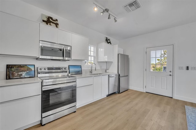 kitchen featuring visible vents, stainless steel appliances, light countertops, light wood-type flooring, and a sink