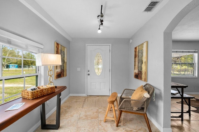 entrance foyer featuring baseboards, visible vents, arched walkways, and a healthy amount of sunlight