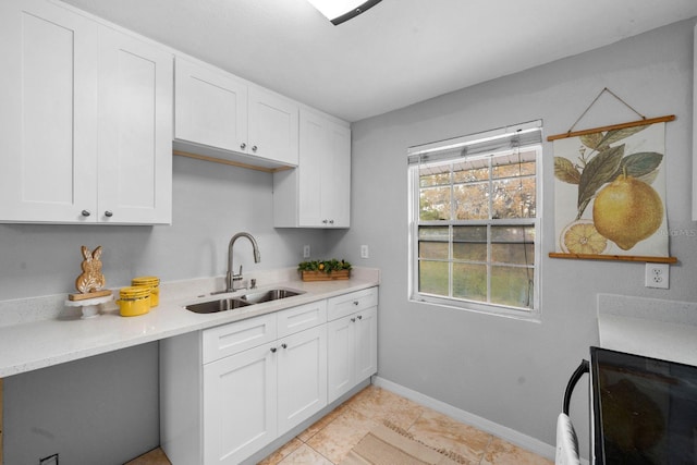 kitchen with baseboards, light countertops, light tile patterned flooring, white cabinetry, and a sink