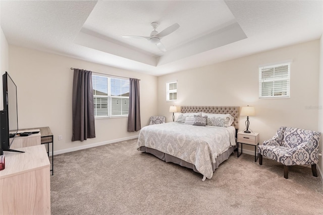 bedroom featuring a tray ceiling, light colored carpet, ceiling fan, and baseboards