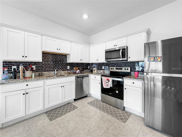 kitchen with white cabinets, light stone counters, stainless steel appliances, and decorative backsplash