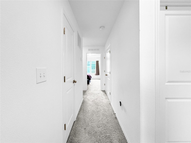 corridor with baseboards, visible vents, and light colored carpet