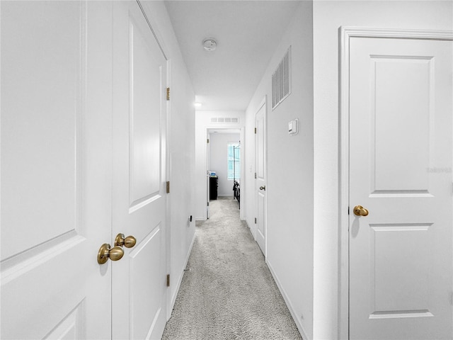 hallway featuring light carpet, visible vents, and baseboards