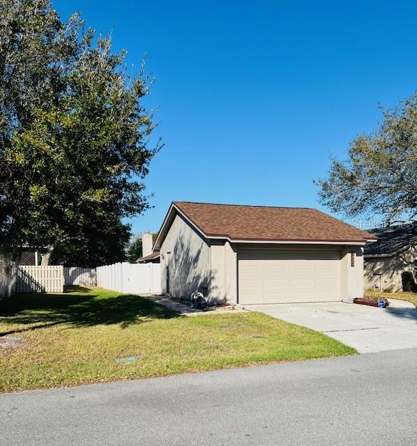 view of side of property featuring a lawn, fence, concrete driveway, and stucco siding