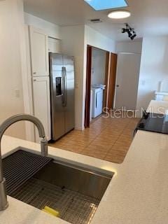 kitchen with light tile patterned floors, a sink, white cabinetry, and stainless steel fridge with ice dispenser