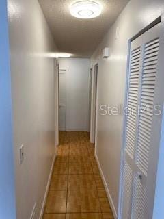 corridor featuring tile patterned flooring, baseboards, and a textured ceiling