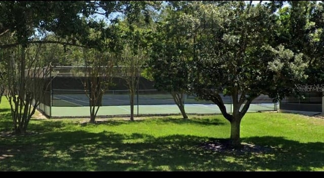 view of property's community featuring a tennis court, a yard, and fence