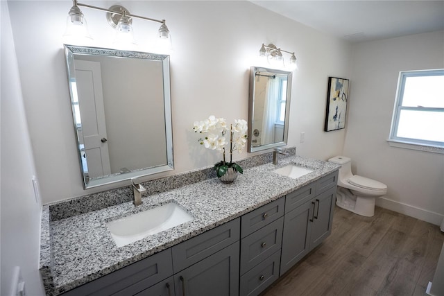 bathroom featuring double vanity, a sink, toilet, and wood finished floors