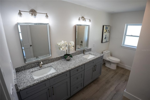 full bath with toilet, double vanity, a sink, and wood finished floors