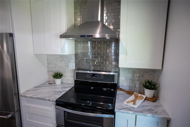 kitchen featuring light stone counters, stainless steel appliances, white cabinets, wall chimney range hood, and tasteful backsplash