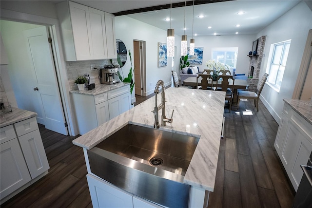 kitchen with dark wood-style floors, light stone counters, decorative backsplash, white cabinetry, and a sink