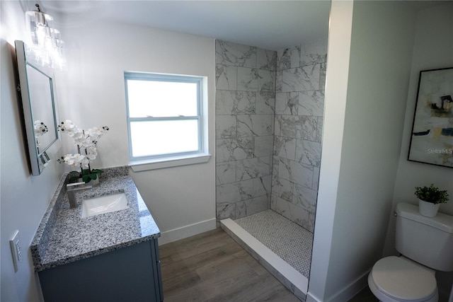 bathroom featuring baseboards, tiled shower, toilet, wood finished floors, and vanity