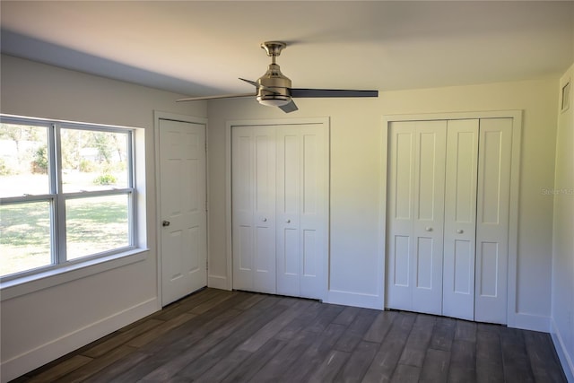 unfurnished bedroom with dark wood-style floors, ceiling fan, baseboards, and multiple closets