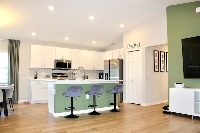 kitchen with lofted ceiling, a breakfast bar area, a kitchen island with sink, stainless steel appliances, and white cabinets