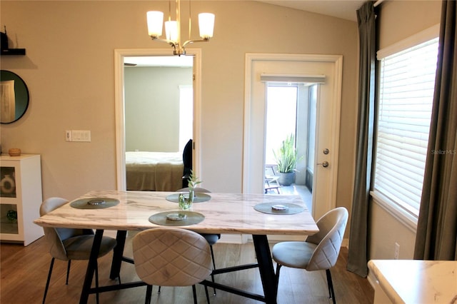 dining area with a chandelier, vaulted ceiling, and wood finished floors