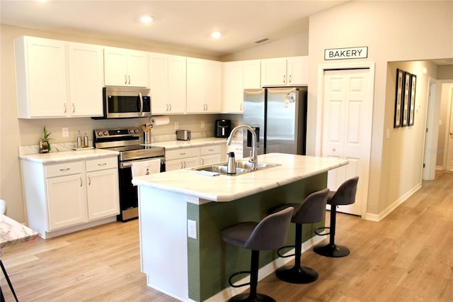 kitchen with light wood-style flooring, stainless steel appliances, a sink, white cabinets, and a kitchen breakfast bar