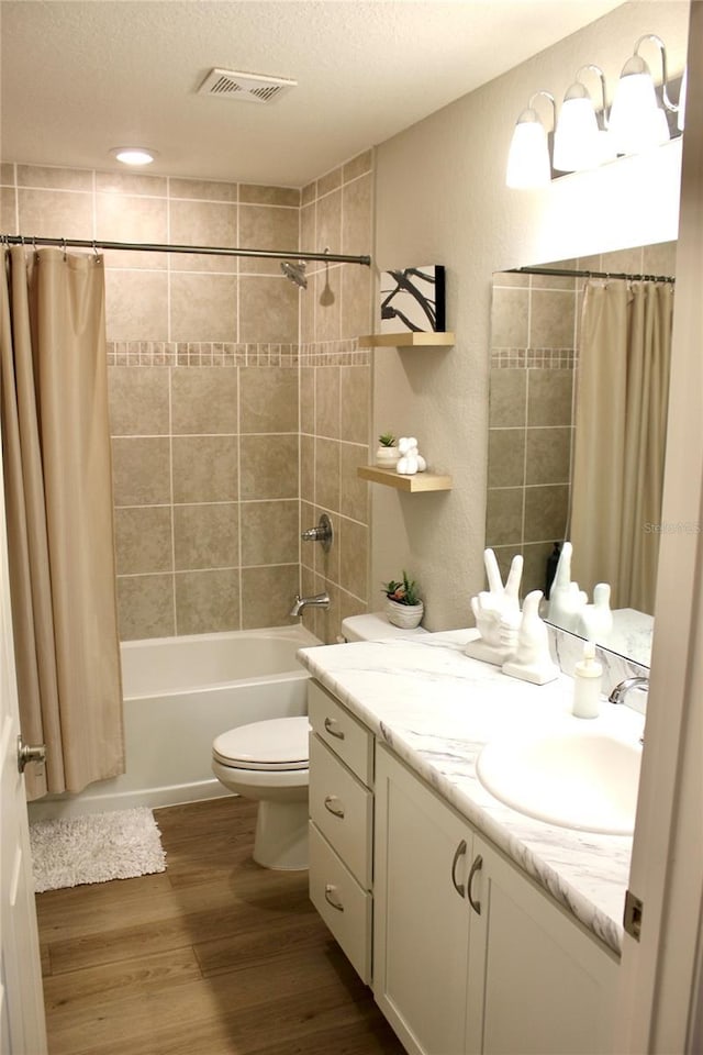 bathroom featuring visible vents, shower / bathtub combination with curtain, toilet, a textured ceiling, and wood finished floors