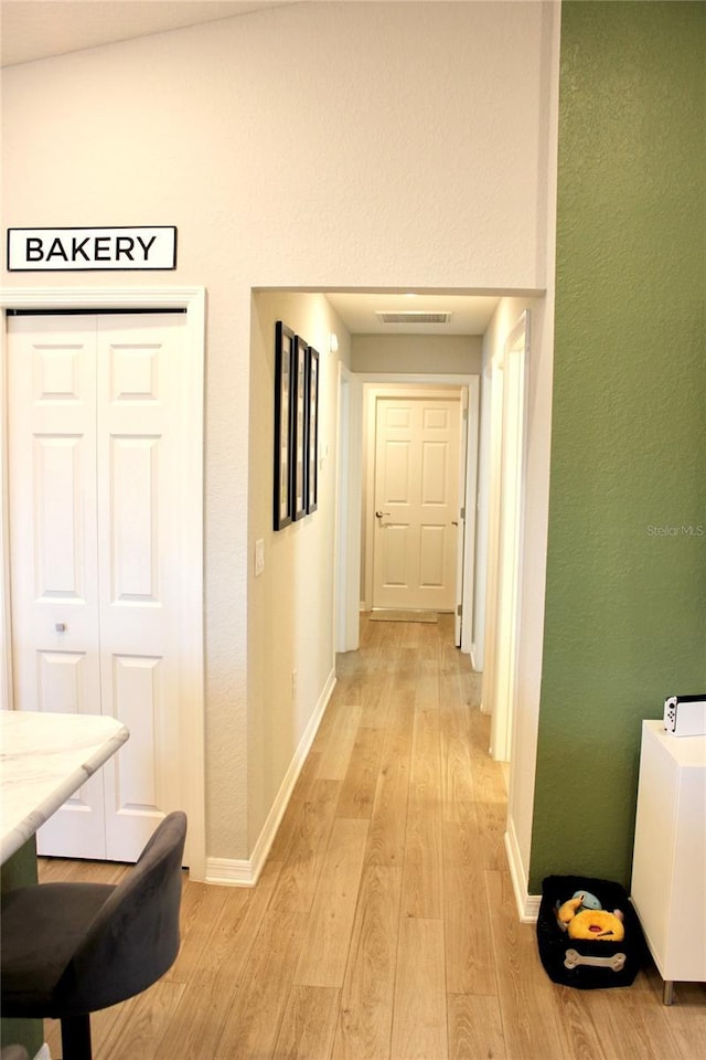 corridor featuring light wood finished floors, baseboards, and visible vents