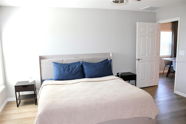 bedroom with baseboards, visible vents, and wood finished floors