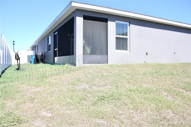 view of property exterior with stucco siding, a sunroom, and a yard