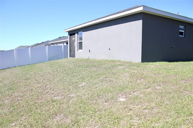 rear view of property with a lawn, fence, and stucco siding