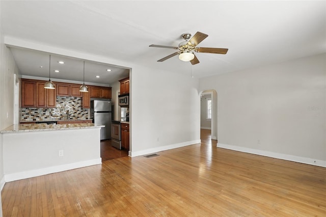 unfurnished living room with visible vents, arched walkways, baseboards, ceiling fan, and light wood-type flooring