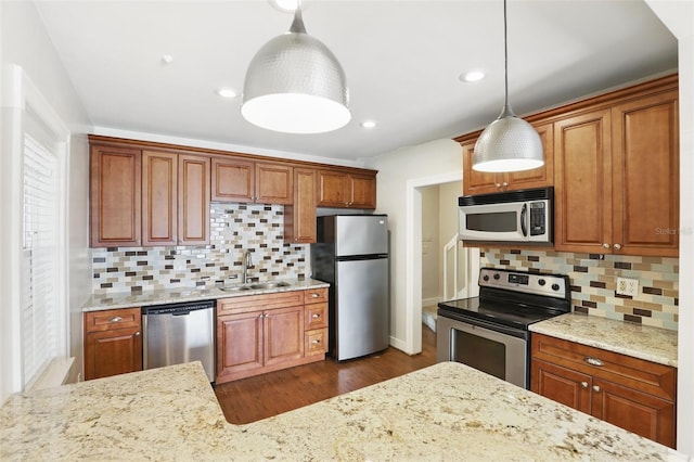 kitchen with stainless steel appliances, backsplash, brown cabinetry, a sink, and light stone countertops