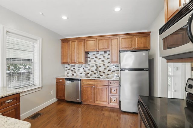 kitchen featuring appliances with stainless steel finishes, brown cabinetry, a sink, and decorative backsplash