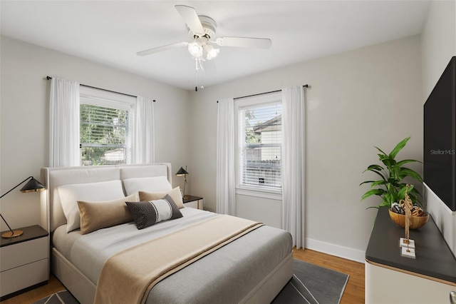 bedroom featuring ceiling fan, multiple windows, wood finished floors, and baseboards