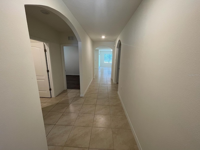 hall featuring arched walkways, light tile patterned flooring, visible vents, and baseboards