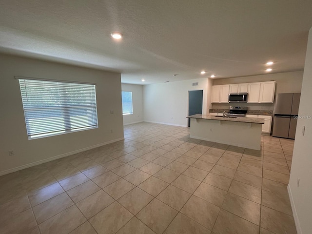 kitchen featuring light tile patterned floors, stainless steel appliances, a sink, white cabinetry, and open floor plan