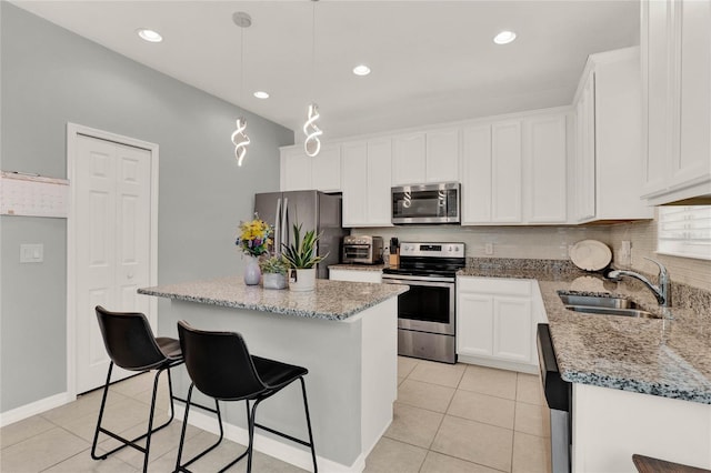 kitchen with light tile patterned floors, appliances with stainless steel finishes, white cabinets, a kitchen island, and a sink