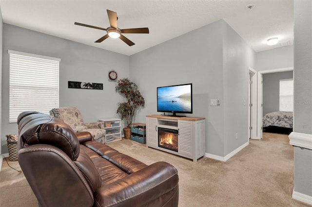 living room featuring light carpet, ceiling fan, baseboards, and a glass covered fireplace