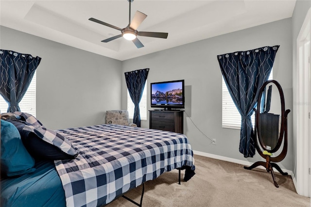 carpeted bedroom with ceiling fan, multiple windows, a raised ceiling, and baseboards