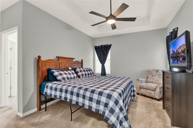 bedroom featuring baseboards, a tray ceiling, a ceiling fan, and light colored carpet