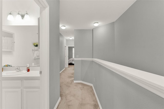 hallway with light colored carpet, a sink, and baseboards