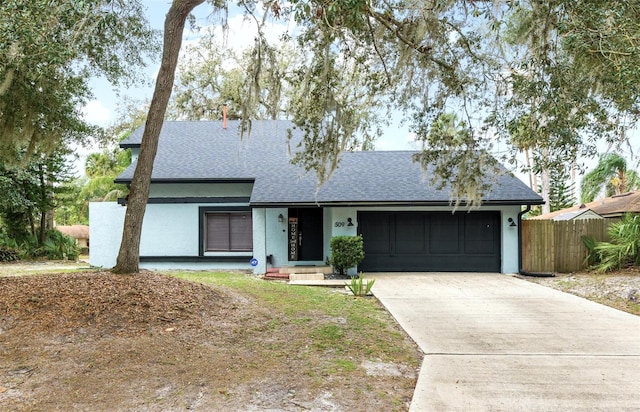 single story home featuring a garage, concrete driveway, roof with shingles, and fence