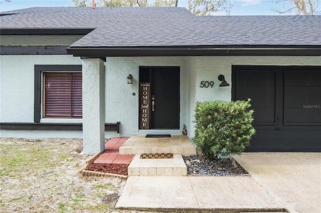 entrance to property with a garage, stucco siding, and roof with shingles