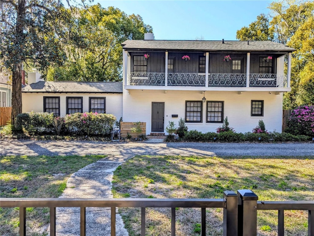 view of front property with a chimney, a balcony, and a front lawn