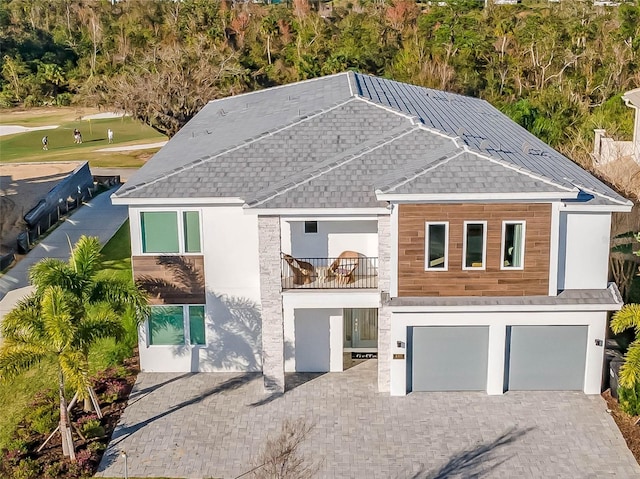 view of front of property featuring decorative driveway, stucco siding, a shingled roof, an attached garage, and a balcony