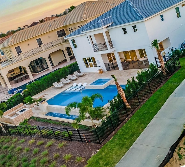 pool at dusk with a patio area, a fenced backyard, and a pool with connected hot tub