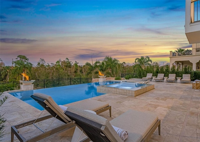 pool at dusk featuring a pool with connected hot tub, a patio, and fence