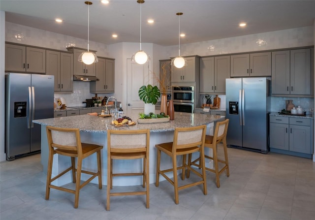 kitchen featuring under cabinet range hood, gray cabinets, light stone counters, and stainless steel appliances