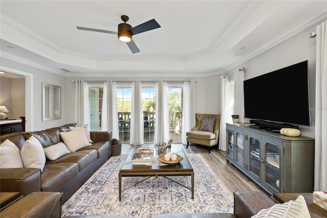 living area with ornamental molding, a tray ceiling, a ceiling fan, and wood finished floors