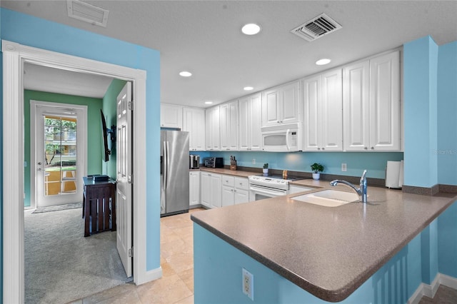 kitchen with a peninsula, white appliances, a sink, and visible vents