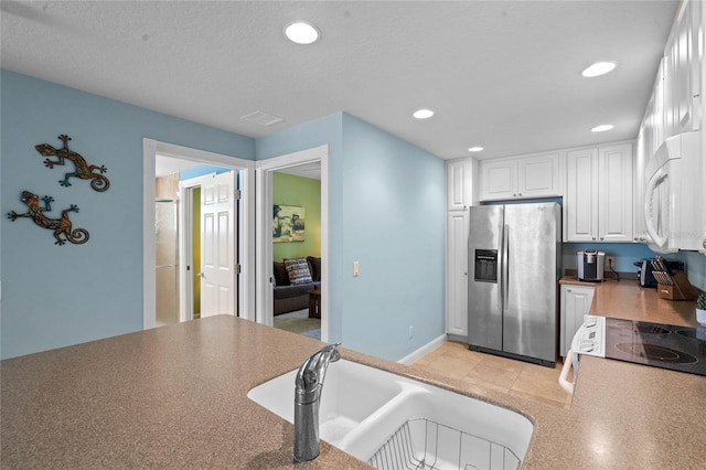 kitchen with recessed lighting, white microwave, white cabinetry, a sink, and stainless steel fridge