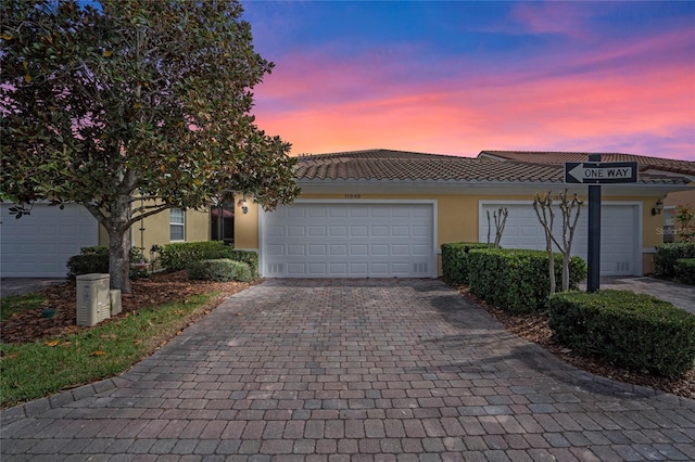 view of front of property with a tiled roof, decorative driveway, an attached garage, and stucco siding