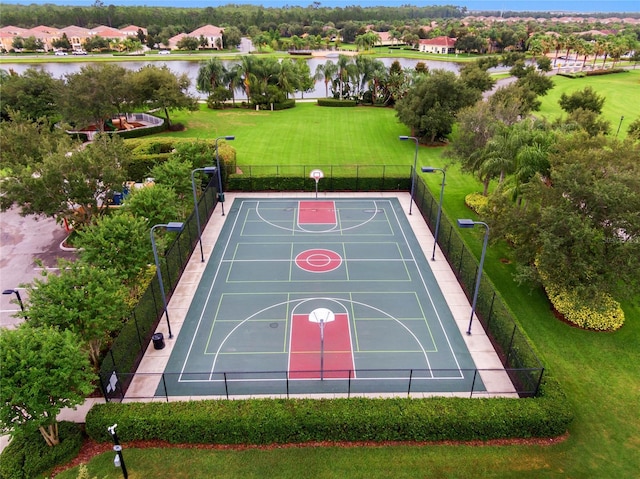 view of sport court with a water view, community basketball court, fence, and a yard